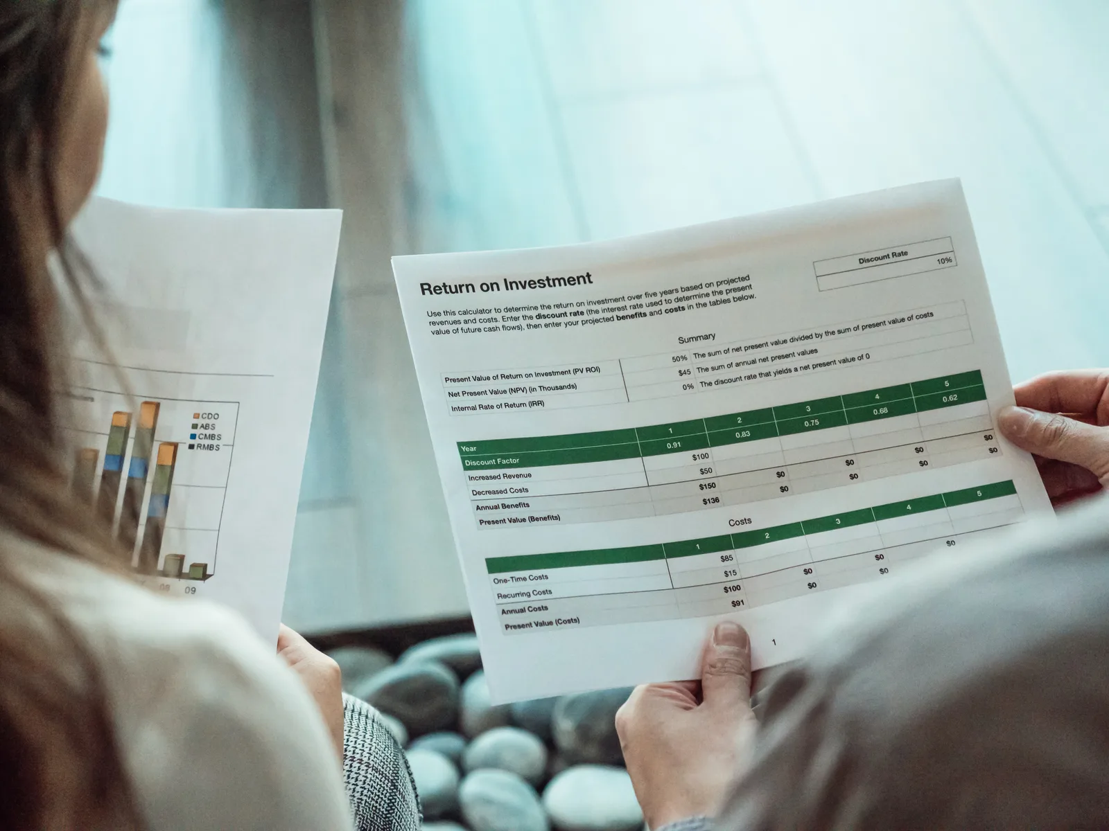 Close-up of two individuals analyzing financial documents related to return on investment.